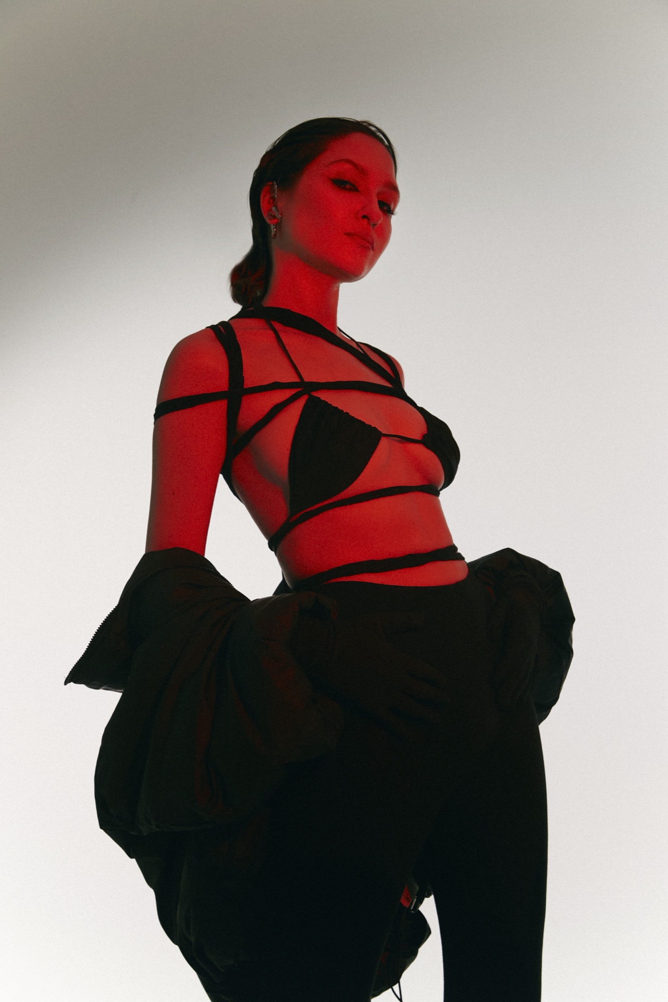 AYGYUL in a black strap top, lit red, shot from below